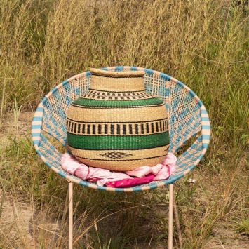 Front view of a tan flower pot basket with green and black designs placed on a pink fabric on top of a blue and tan chair