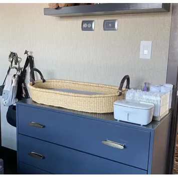 Handwoven bassinet baby changing basket in tan on a blue console.