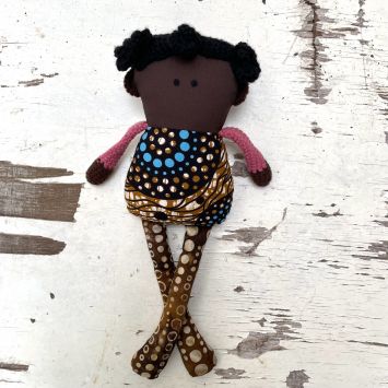 Flatlay of an Akili Wiz Buddie Girl doll wearing mult-colored clothing