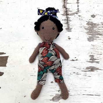 Flatlay of a Rafiki Mwenzi Girl doll wearing a multi colored romper and headwrap