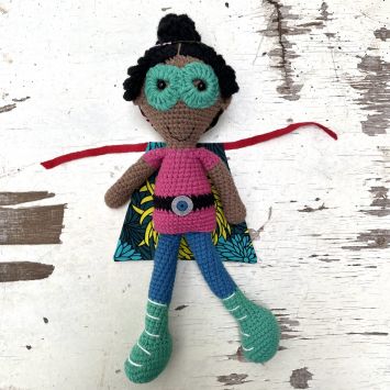 Flatlay of a Rafiki Mwenzi Superhero Girl doll wearing a multi colored outfit