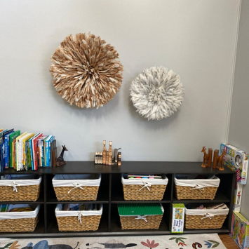 Beige and Cream Bamileke Juju Hats  on the wall above a bookshelf with books and organisation woven baskets