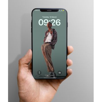 A phone being held out. The lockscreen is a man with his hands inside his pockets, wearing an unbuttoned shirt revealing his white undershirt