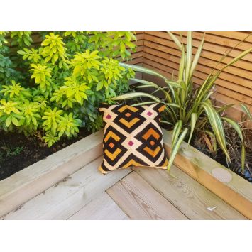 Top view of a multi-colored decorative Kuba cushion placed outdoors next to plants
