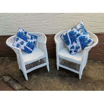 Front view of two white cane and bamboo single seater chairs placed outside with a blue and white pillow on each