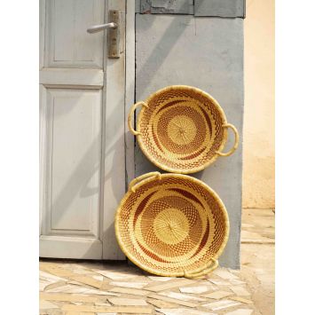 Front view of two tan and orange Koleke baskets placed on their side next to a wall