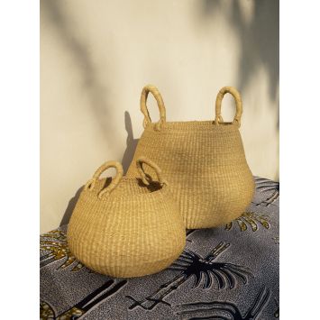 Two tan Bolo Woven Basket with Handles in different sizes next to a wall